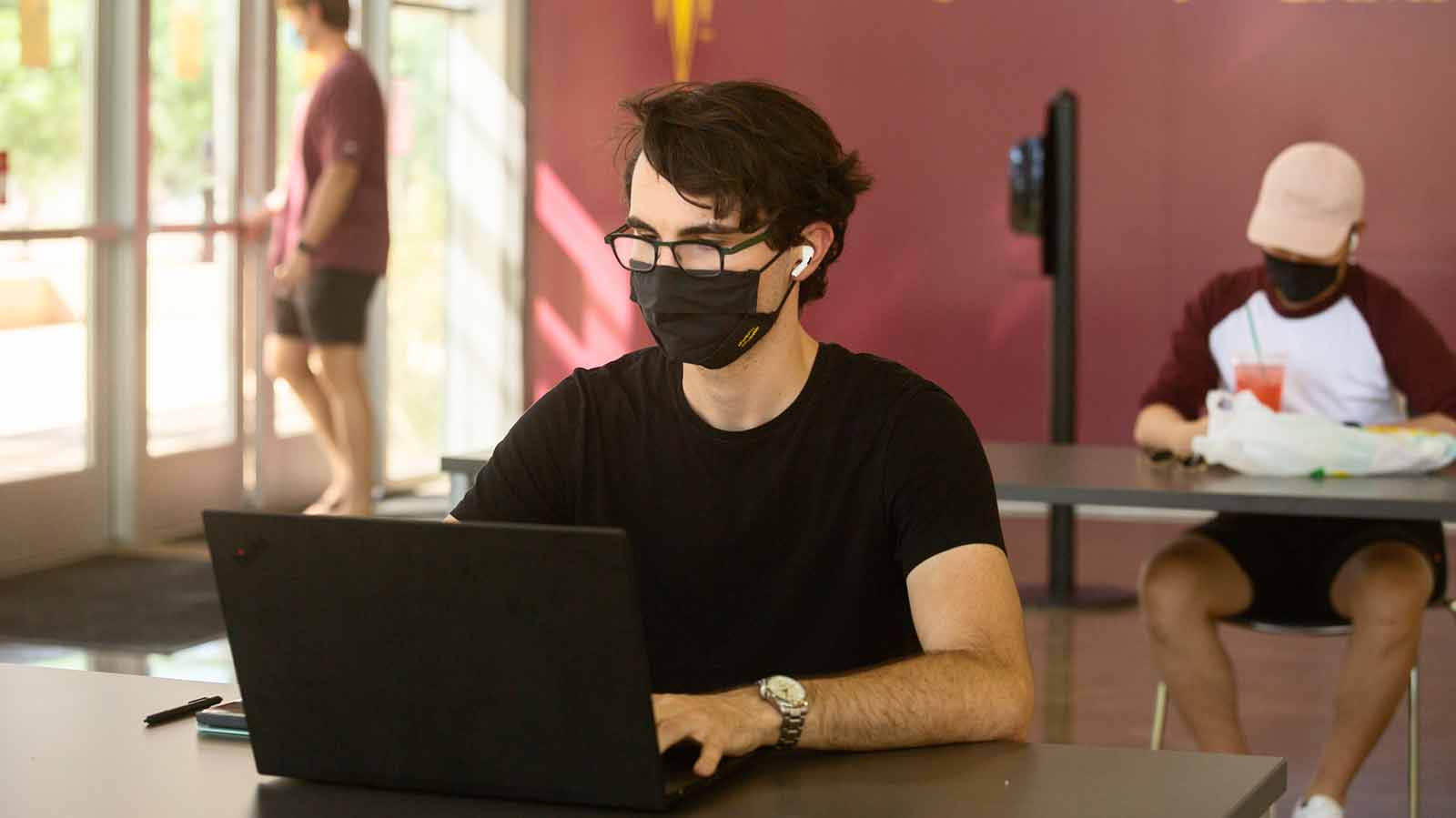 Male student wearing a mask while using a laptop.