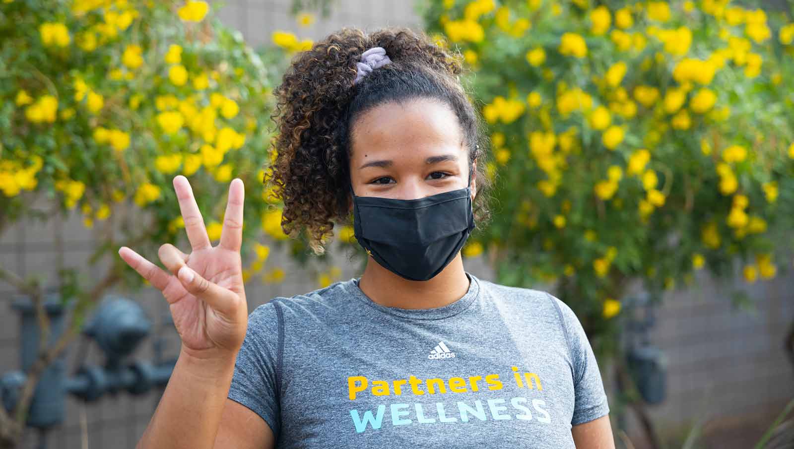 Female student wearing a mask and showing forks up hand sign